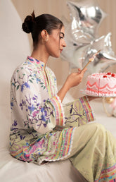 Woman in a colorful outfit holding a cake with balloons in the background